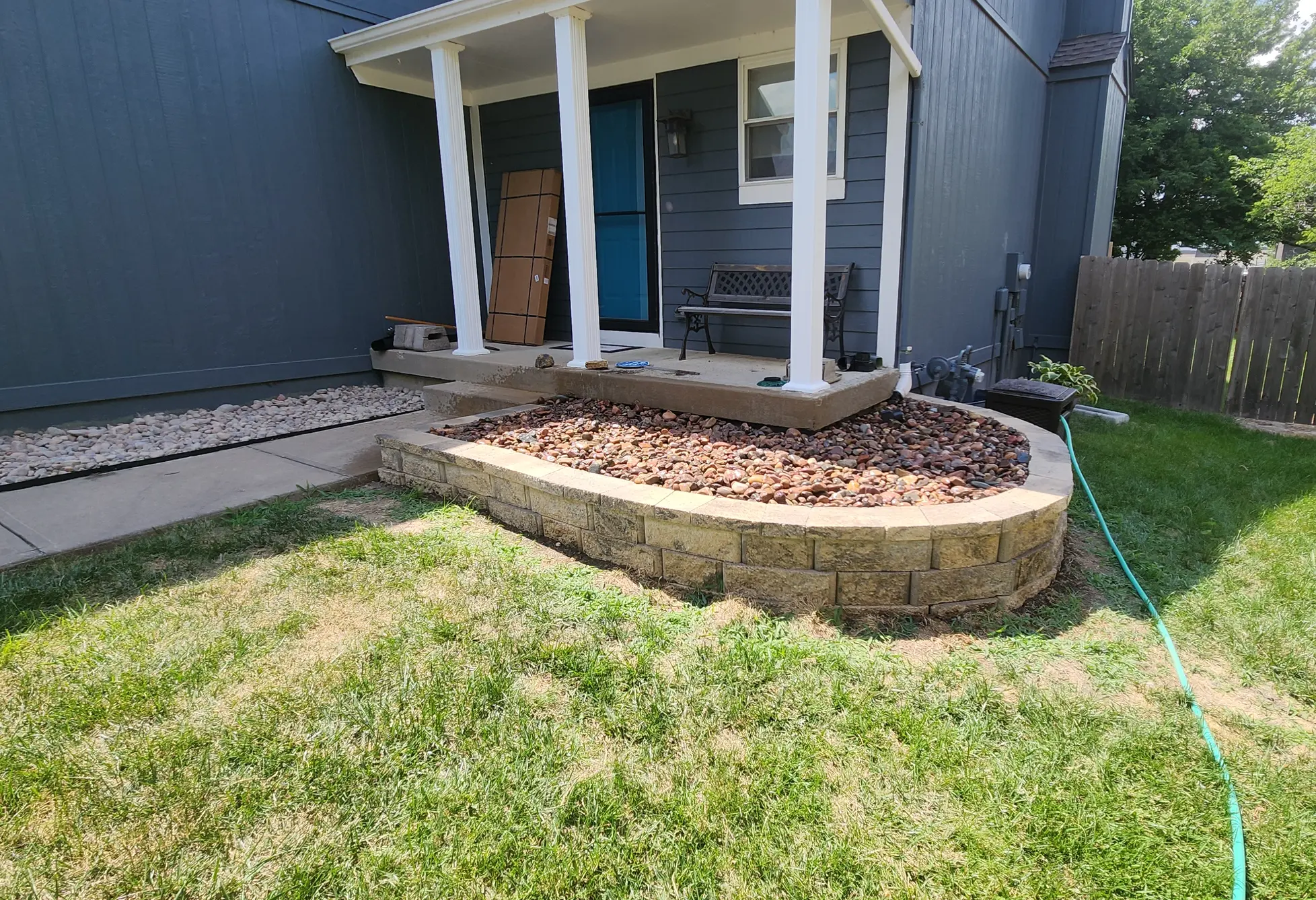 Finished raised stone bed and river-rock landscaping beside a front porch in Olathe