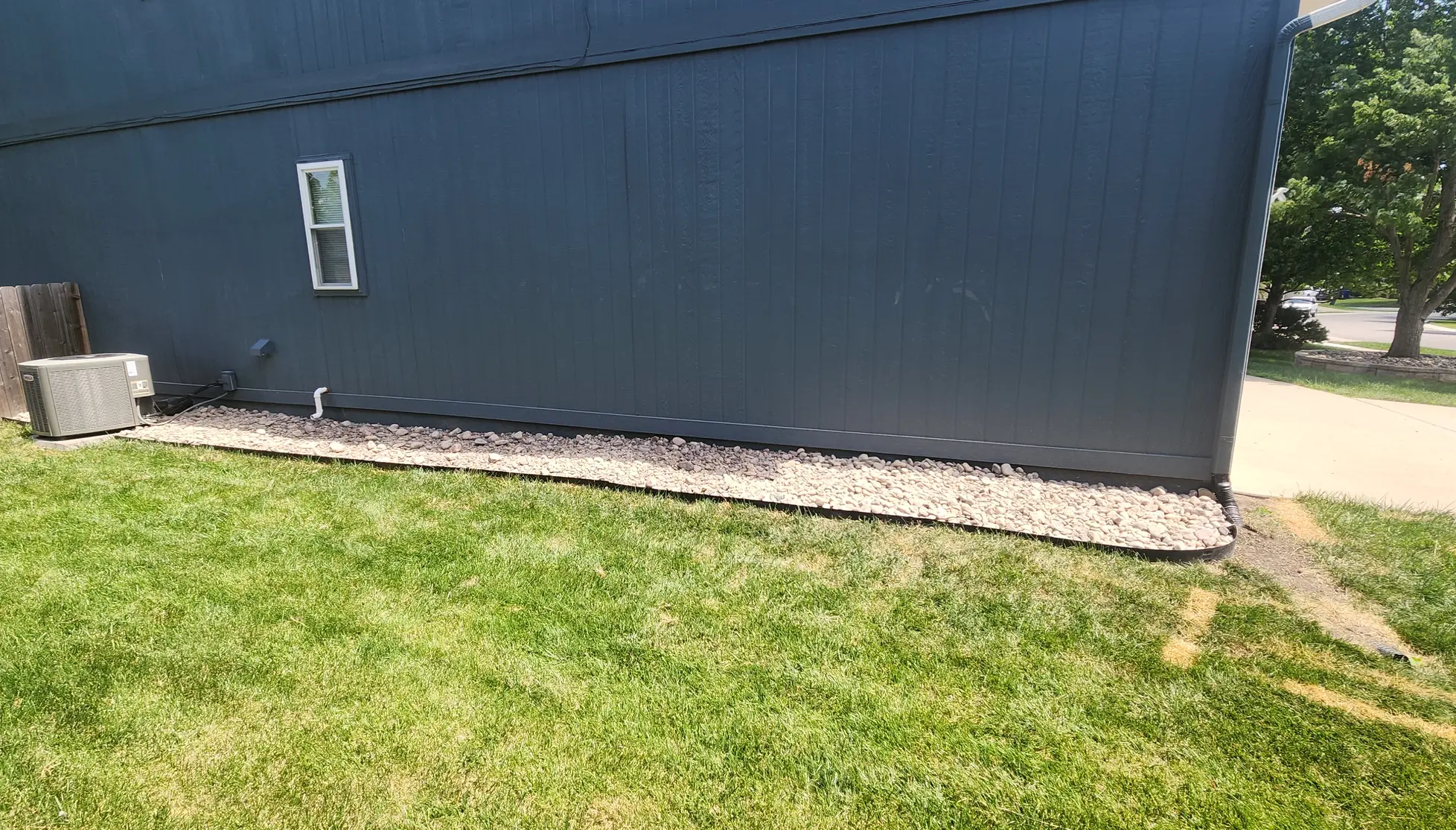 Long decorative stone bed with metal edging along the side of a home